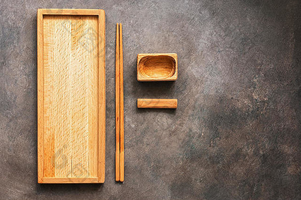 一套木制菜肴和餐具亚洲料理寿司和面包卷，一个长方形盘子，筷子和一个深色背景的酱油碗。顶v