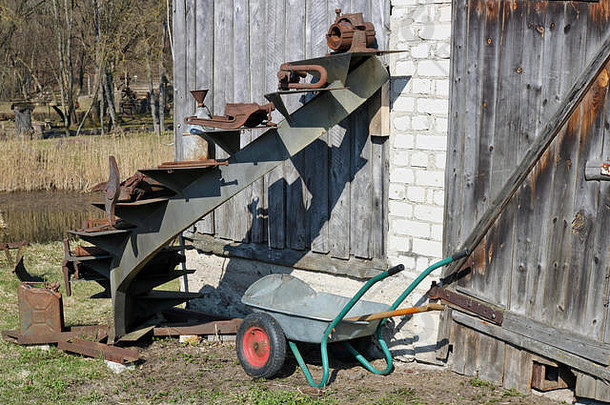 废弃的破碎乡村谷仓附近的柴油罐和手动花园独轮车乡村景观