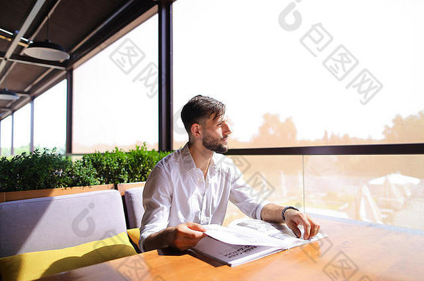 英俊的<strong>插</strong>画家在餐桌旁观看杂志图片。