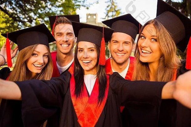 兴奋的五位成功的快乐的五位毕业生穿着长袍，戴着流苏一起自拍