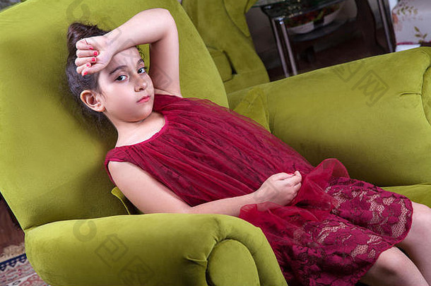 可爱可爱的中东女孩，穿着<strong>深红</strong>色连衣裙，留着浓密的头发，在家里的绿色沙发上摆着姿势和李英。