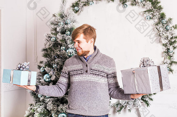 快乐的年轻人在圣诞树的背景上拿着两个礼品盒