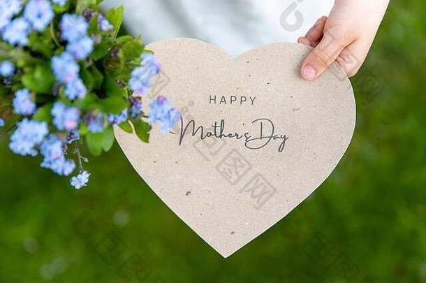 母亲节快乐写在一张心形卡片上，一个女孩在草地上举着“勿忘我”