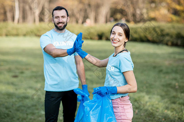 公园清洁后，一位身穿蓝色t恤的快乐志愿者手拿垃圾袋站在那里，给了五个人一张照片