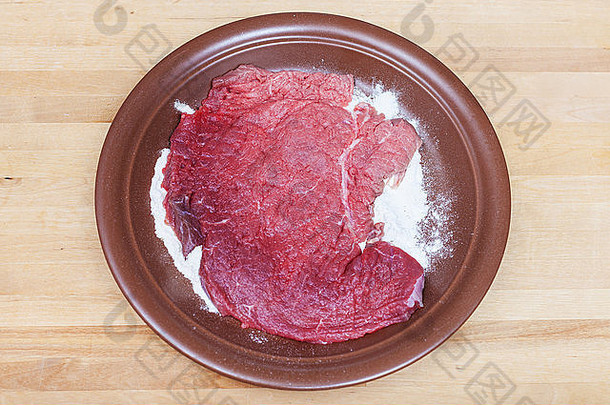 木制桌子上盘子上涂有面粉的嫩生小牛肉排俯视图