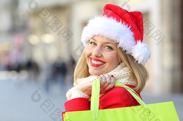 一个戴着圣诞老人帽子的快乐女孩在圣诞节购物，看着你在街上的户外