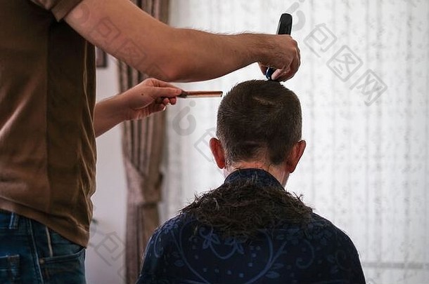 在家中进行冠状病毒隔离期间，这名年轻人正在用理发器为父亲理发。家庭理发概念。