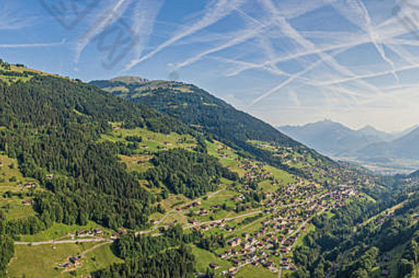 阿尔卑斯山谷和郁郁葱葱的松林上空的航空影像，山谷周围有小屋和高山。