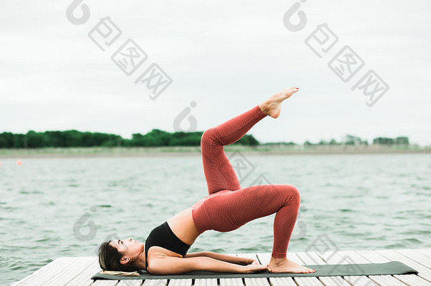年轻的亚洲女孩瑜伽在户外码头湖她是穿黑色的前红色的紧身裤