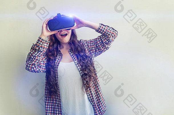 在白色背景下，戴着虚拟现实VR眼镜和头盔耳机的年轻女子微笑。智能手机使用虚拟现实护目镜。技术、模拟、高科技、电子游戏概念