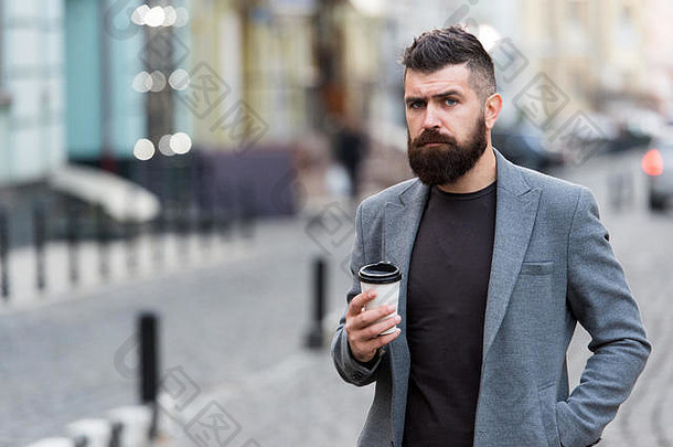男人留胡子的时髦人士喝咖啡纸杯。打扮得体的商人在城市背景下享受户外咖啡休息。喜欢边走边喝咖啡。体贴但放松。照顾好自己。美味的饮料。