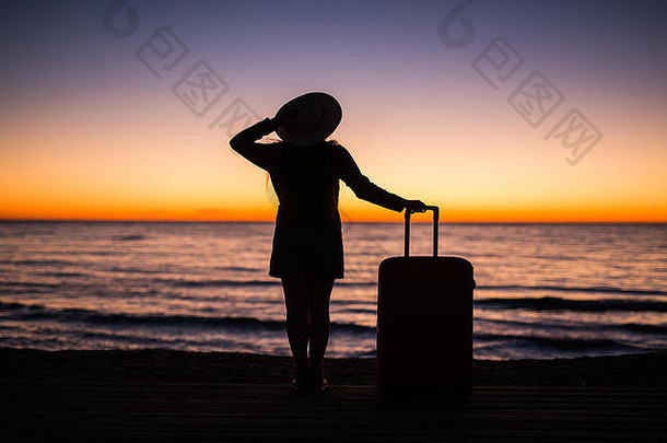 旅游、度假和暑期旅行概念-穿着夏装、戴着夏帽的年轻女子的剪影，面向大海