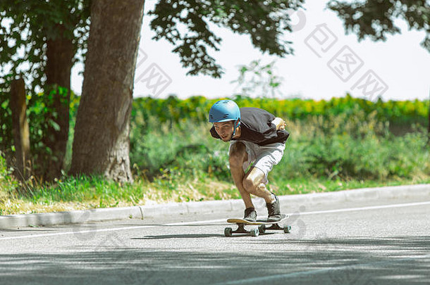 在阳光明媚的日子里，滑板手在草地附近玩滑板。年轻人在装备上骑行，在柏油路上玩长板。休闲活动、运动、极限、爱好和运动的概念。