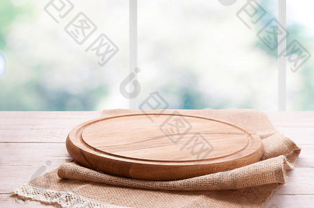 空的有纹理的木制比萨饼板，桌上有餐巾，厨房窗户背景模糊