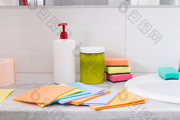 浴室里，一套五颜六色的家用清洁布沿着洗手盆摊开，后面是海绵和肥皂