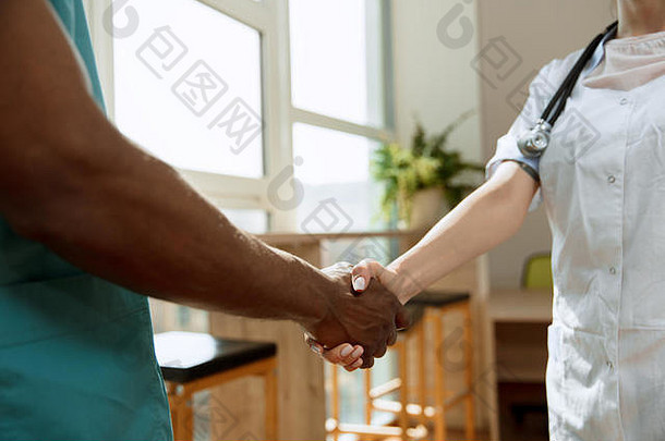 医学合作的概念。两名医生在灰色医院背景上握手的特写照片。关于医疗保健、健康、诊所、医药和团队合作的广告形象。