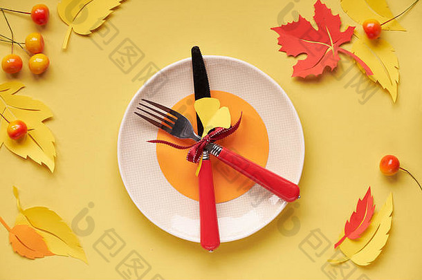 秋季庆典、感恩节或生日的餐桌设置。明亮的塑料板，用叉子和刀子放在黄色的纸上，纸上有秋天的叶子和叶子