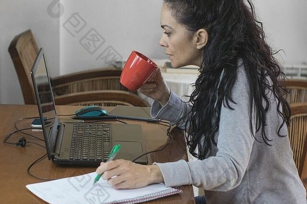 布鲁内特妇女在家里为COVID-19远程办公，看电脑和喝咖啡
