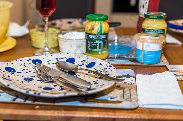 在木制餐桌上吃完食物后，用叉子、勺子和刀清空用过的彩色盘子。