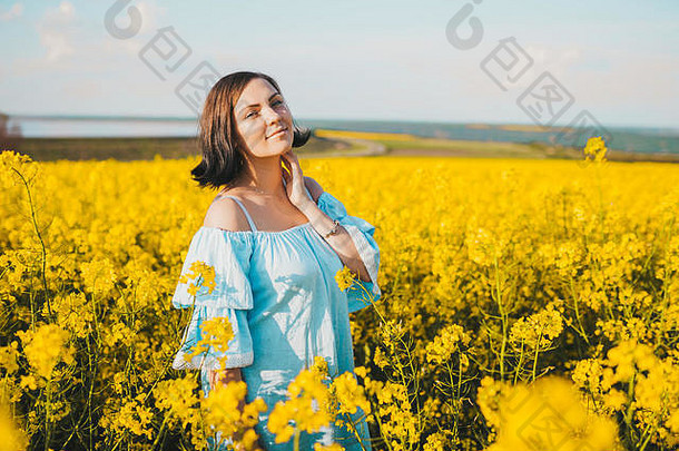 身着蓝色连衣裙的美丽女子在油菜黄色花圃中摆姿势的肖像