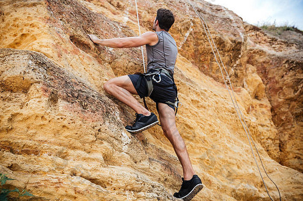 年轻英俊的运动员攀登岩石悬崖