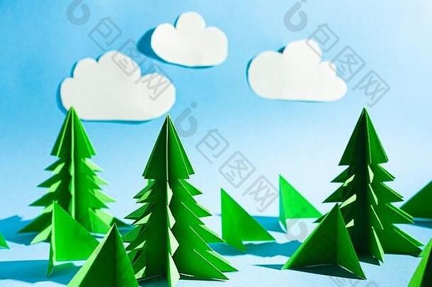 折纸森林景观。绿色的圣诞树，松树，蓝天白云。用纸做的针线活。股票照片。