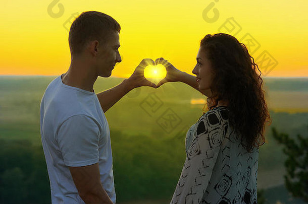日落时分，这对年轻的情侣用手做了一个心形，阳光透过双手，美丽的风景和明亮的黄色