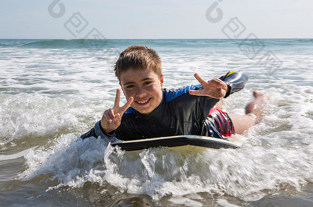 英国威尔士，一个小男孩脸上挂着灿烂的笑容在冲浪板上冲浪。