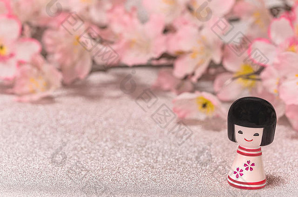 日本新年贺卡上印有小洋娃娃Kokeshi的图案，在闪亮的银色背景上有樱花枝。
