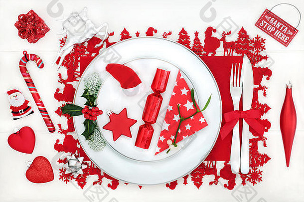 圣诞晚餐有趣的桌子，白色木质桌子背景上有瓷盘、装饰品、餐巾、餐具和冬季植物。节日的