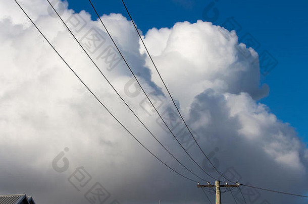 在晚秋一个阳光明媚的下午，郊区的电线和电线杆上有蓬松的白色积云和一些积雨云。