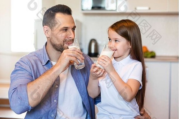 爸爸和小女儿在家的厨房里喝牛奶