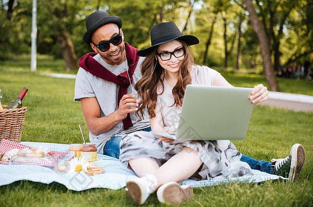 微笑的年轻夫妇在户外听音乐和使用笔记本电脑