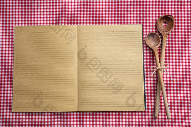 烹饪食谱。红色桌布上的空白笔记本和木制厨房用具，俯视图，复印空间
