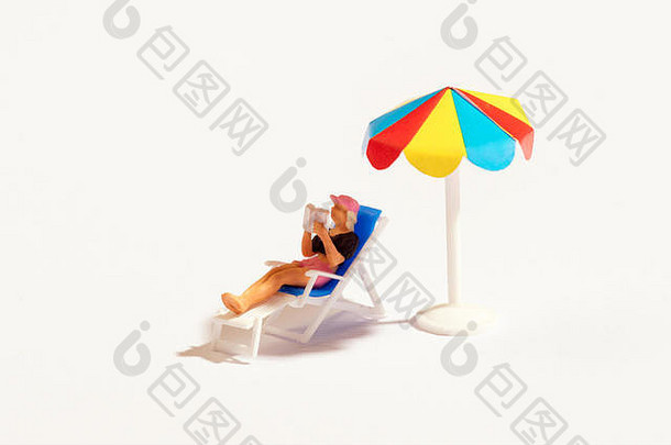 微型人在躺椅上看书，在白色的沙滩伞下晒日光浴
