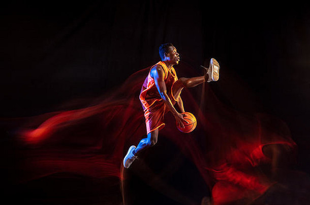越来越高，越来越强。在黑暗的演播室背景下，红队的非洲裔美国年轻篮球运动员正在比赛，霓虹灯闪烁。运动、运动、活力和健康生活方式的概念。