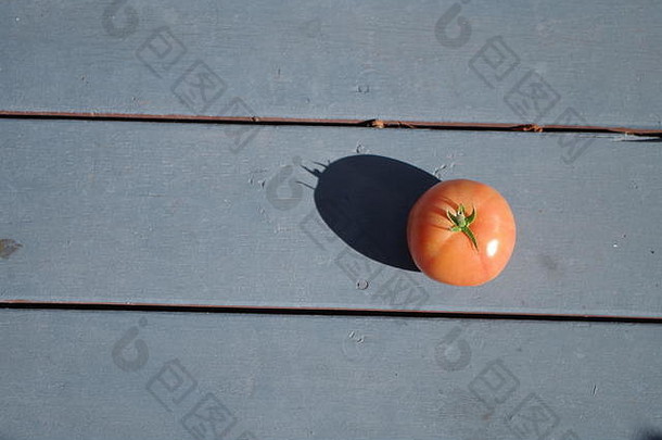 一个西红柿投下了一个阴影到一个蓝色油漆木背景，极简主义的照片。