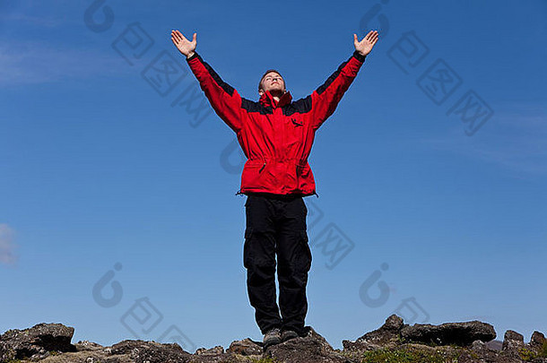 一名男子在山顶伸出双臂庆祝成功。