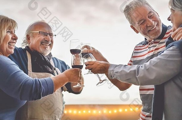 快乐的老年朋友在阳台上喝红酒日落-成熟的人在户外欢笑和分享时间