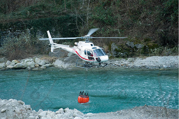 直升机从山河中收集水桶中的水用于灭火和灭火，飞机的特写镜头