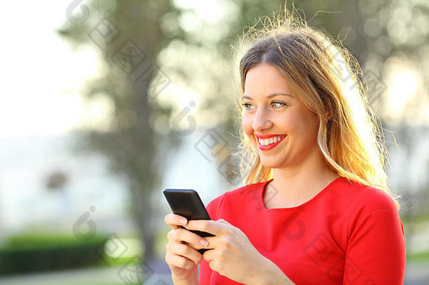 在海滩附近的一个公园里，一个手持智能手机的快乐女孩在一旁看着