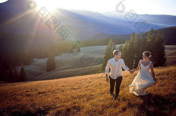 美丽的新婚夫妇在群山环绕的田野上奔跑和嬉戏