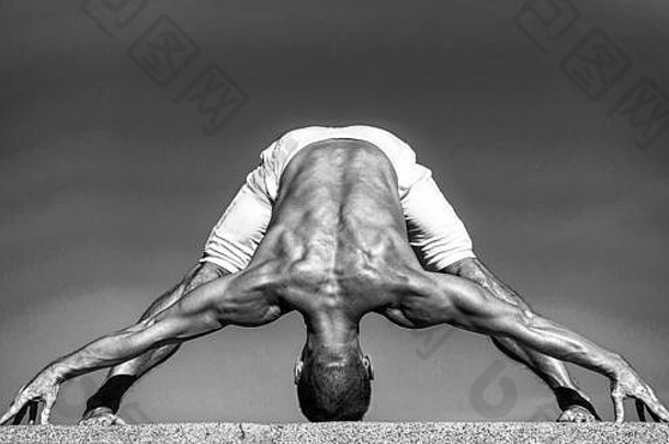 在瑜伽中，保持年轻的关键是灵活的脊柱。瑜伽教练用肌肉做运动。<strong>身心健康</strong>。肌肉发达的男子处于瑜伽姿势。运动和保健，黑白相间。