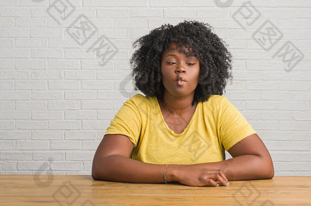 年轻的非裔美国妇女坐在家里的桌子上，用嘴唇做鱼脸，疯狂而滑稽的手势。滑稽的表情。