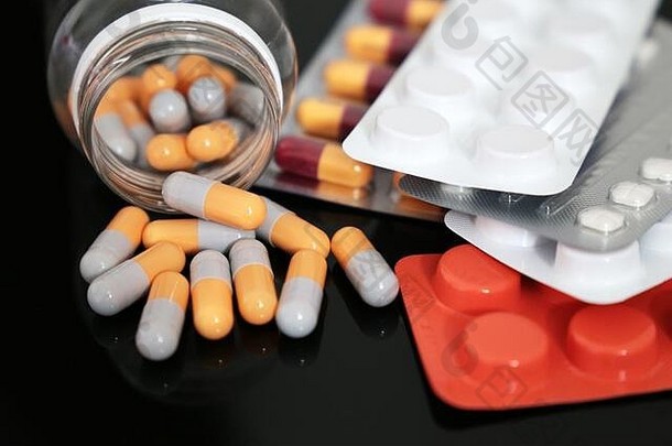 黑色玻璃桌上的药片、药片和胶囊从瓶子里散落。<strong>冠状病毒防护</strong>、药学、抗生素的概念