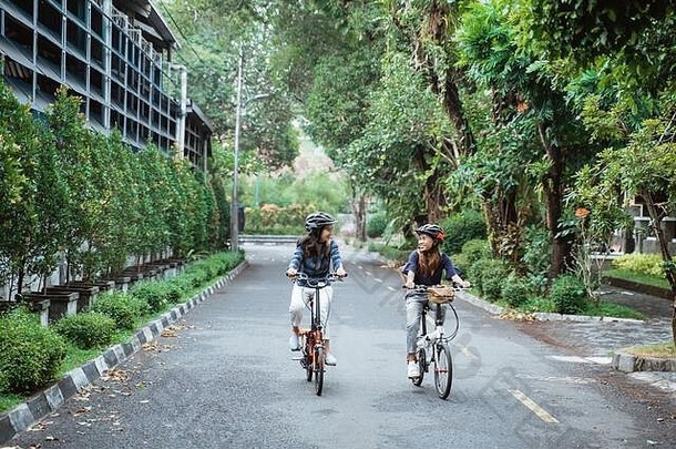 两名亚洲妇女戴着头盔和提包骑自行车