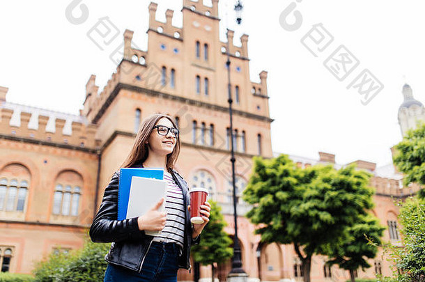 大学背景下背着背包的快乐女生。午餐休息时，一位女士拿着作业本和外卖咖啡在校园休息。