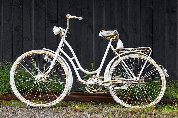 黑色的木墙上挂着一辆白色的生锈的旧自行车。复古背景。水平的