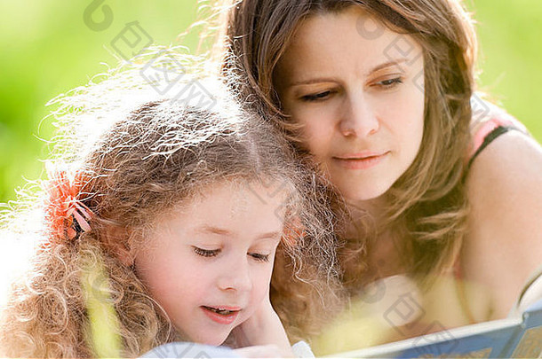 美丽的女孩阅读书妈妈。微笑夏天公园背景
