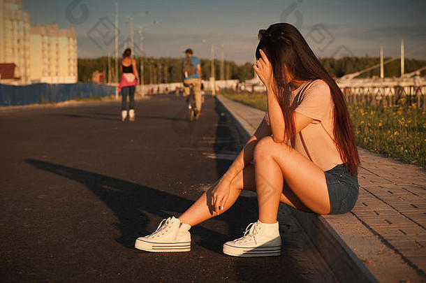 炎热晴朗的日子里，穿着短裤坐在路边的亚洲女孩